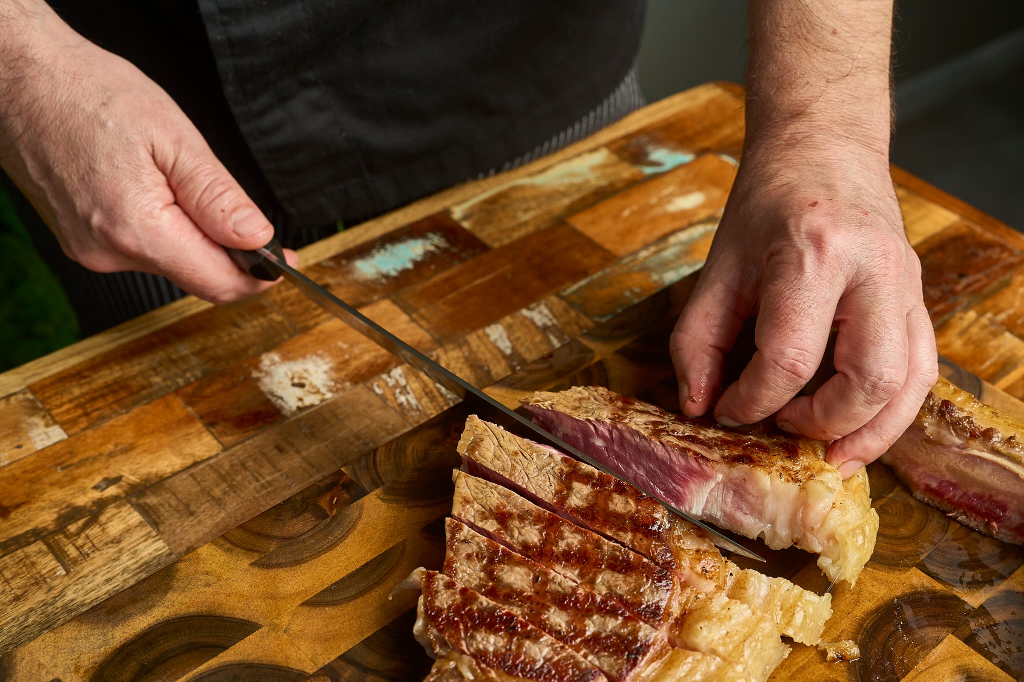 Lo chef di Komos taglia una costata alla griglia sul tagliere
